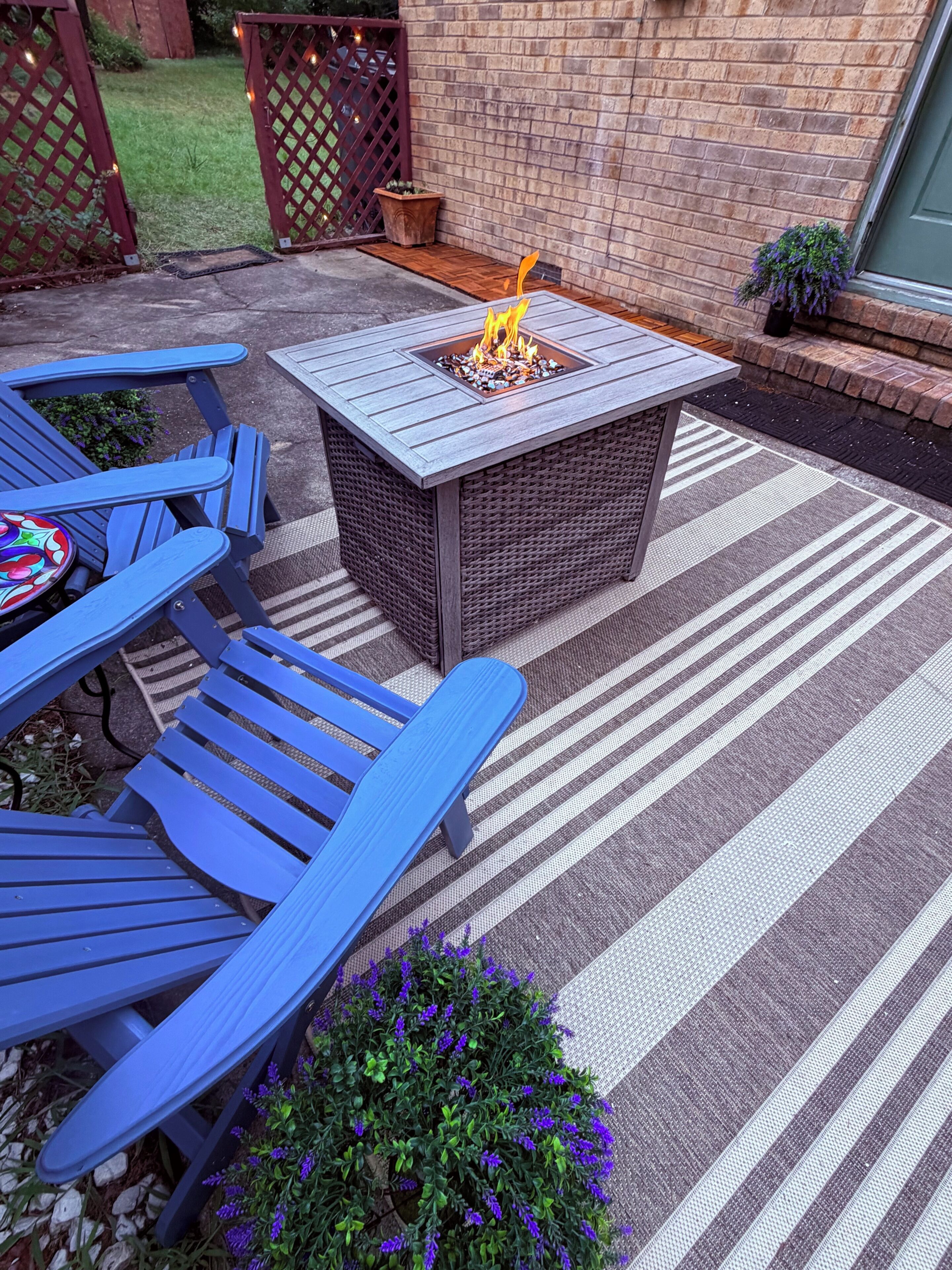 A patio area with a fire pit, blue chairs, and a striped rug.