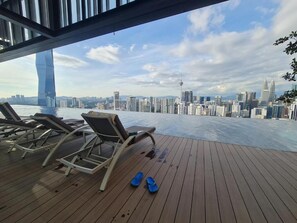 Une terrasse dotée de chaises longues et d’une paire de pantoufles bleues, offrant une vue sur un paysage urbain dominé par une tour imposante.