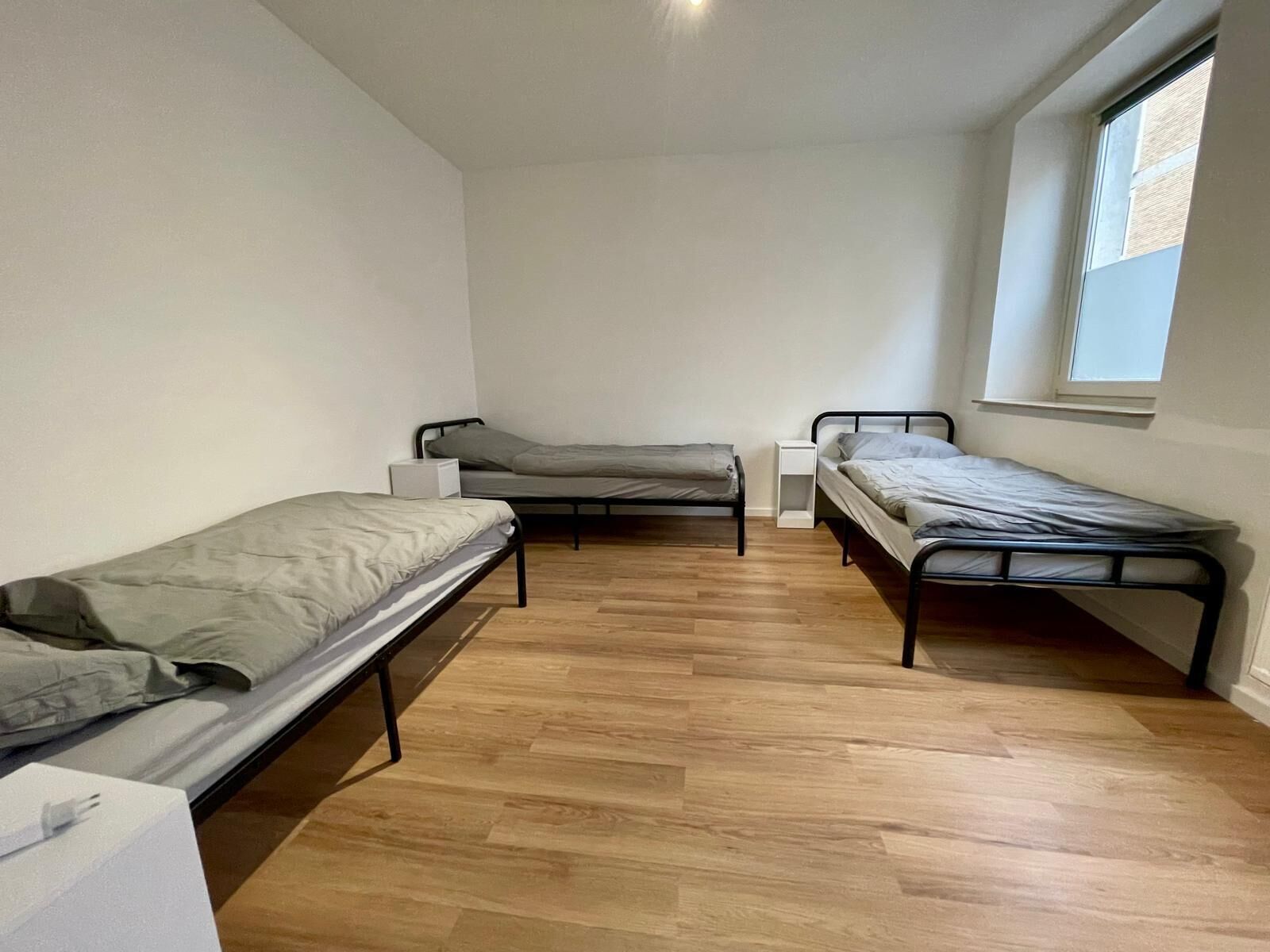 Ein kleiner, einfach eingerichteter Raum mit zwei Einzelbetten, einem Fenster und Holzboden.