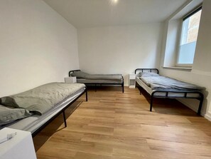 A small, sparsely furnished room with two single beds, a window, and a wooden floor. - Krefeld HomeBase with kitchen and 3 single beds—centrally located near Düsseldorf (Krefeld)
