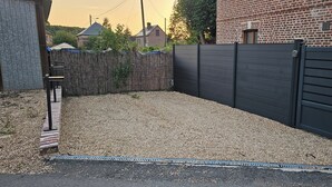 En inhägnad trädgård med grus, ett trästaket och en byggnad i tegel som syns i bakgrunden.