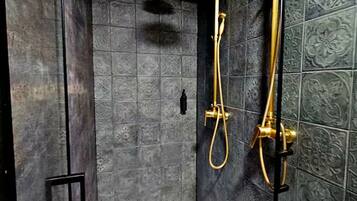 Eine Dusche mit goldfarbener Duschbrause und Duschschlauch, vor dunklen, gemusterten Fliesen.