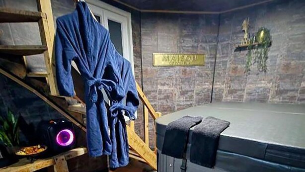 Ett rum med en massagestol, ett massageställ, en trätrappa och en skylt med texten ”MAISON”.