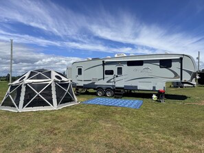 A recreational vehicle with a covered area and a blue mat on the ground.