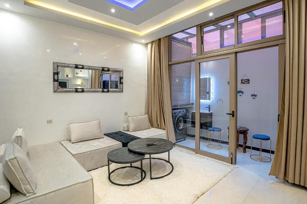 Een moderne woonkamer met een bank, twee ronde tafels, een grote spiegel en een glazen schuifdeur naar een wasruimte.