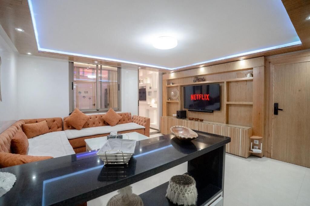 A modern living room with a sofa, a coffee table, a flat-screen TV mounted on a wooden wall, and a fireplace.