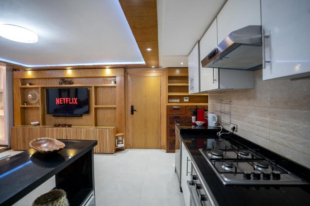 Een moderne keuken met een ingebouwde televisie waarop 'NETFLIX' staat, een fornuis en houten kastjes.