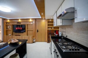 A modern kitchen with a built-in TV displaying 'NETFLIX,' a stove, and wooden cabinetry. - Cozy Sh'Amira Duplex Apartment in Semlalia (Marrakech)