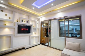 A modern living room with a flat-screen TV, built-in shelving, and a glass door leading to a kitchen. - Cozy Sh'Amira Duplex Apartment in Semlalia (Marrakech)