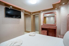A hotel room with a bed, a TV mounted on the wall, a mirror above the sink, and a shower area. - Cozy Sh'Amira Duplex Apartment in Semlalia (Marrakech)