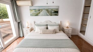 A bedroom with a bed, two bedside tables, a nightstand, a window with curtains, and a wall-mounted picture.