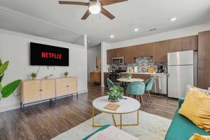 A modern living room with a flat-screen TV, a dining area with a round table, and a kitchen with stainless steel appliances. - Midtown Dallas Escape | 1BR 1BA Suite | Pool | Free Parking (Dallas)
