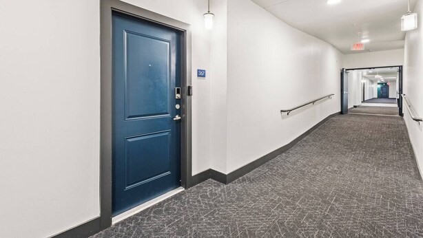 Um corredor com uma porta azul, uma placa de número e um corrimão.