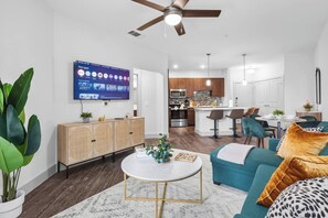 Ein modernes Wohnzimmer mit Fernseher, einer Couch, einem Couchtisch und einem Essbereich mit Stühlen.