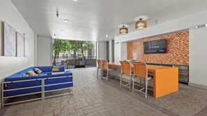 Um interior moderno com um sofá azul, cadeiras laranja, uma televisão e uma parede estampada.
