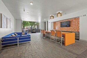 Ein modernes Interieur mit einem blauen Sofa, orangefarbenen Sesseln, einem Fernseher und einer Wand mit Muster.
