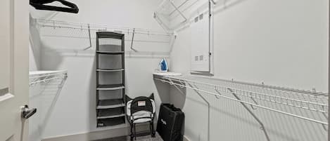 A compact storage room with metal shelving units for hanging items, a small bench, and a door.
