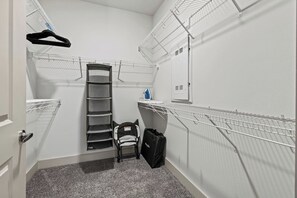Een kleine opslagruimte met metalen schapunits om spullen aan op te hangen, een klein bankje en een deur.