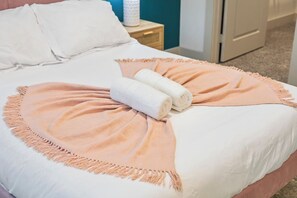 Ein Bett mit einer pfirsichfarbenen Decke und aufgerollten weißen Handtüchern.