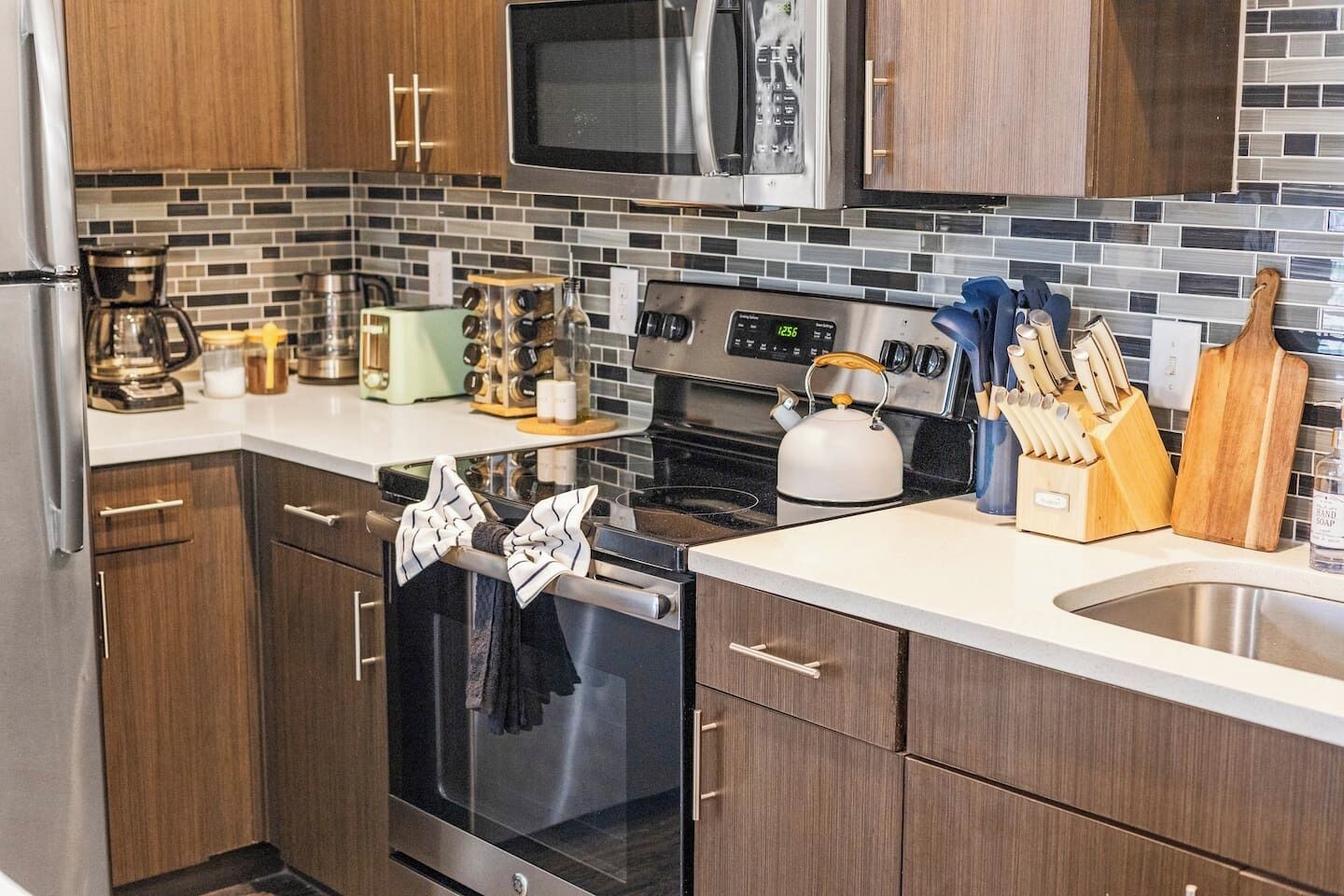 Una cucina moderna con mobili in legno, un frigorifero in acciaio inossidabile, un forno a microonde, un forno e un bollitore.