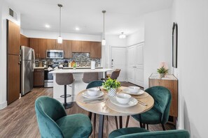 Una cocina moderna con electrodomésticos de acero inoxidable, una isla central con asientos y un comedor con una mesa redonda y sillas verdes.
