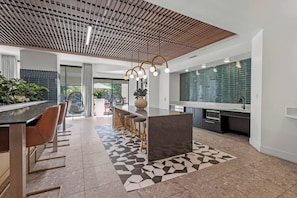 A modern kitchen with a central island, bar seating, and a patterned rug. - Luxury 1BR | Midtown Dallas | Pool, Gym, Free Parking (Dallas)
