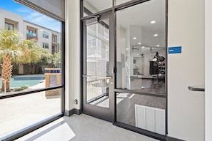 A hotel entrance with a glass door leading to a pool area and a gym. - Luxury 1BR | Midtown Dallas | Pool, Gym, Free Parking (Dallas)