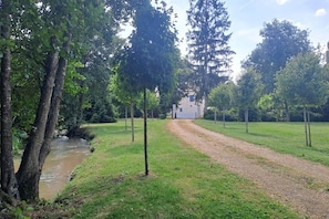 A gravel path leading to a building surrounded by trees and a small stream.