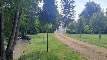 Un chemin de gravier mène à un bâtiment entouré d’arbres et bordé d’un petit plan d’eau.