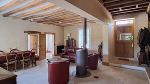 A spacious living room with a high ceiling, a fireplace, a dining area with chairs, and a door leading outside.