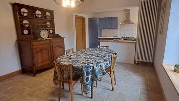 Un coin repas avec une table, des chaises, un buffet en bois contenant de l’assiette, et une cuisine en arrière-plan.