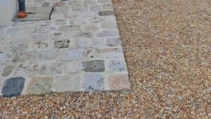 A building with a stone pathway leading to a door, a gravel area, and a hedge.