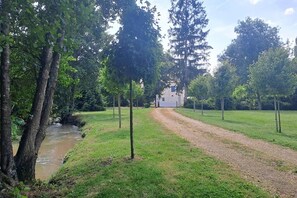 A gravel path leading to a building surrounded by trees and a small water body.