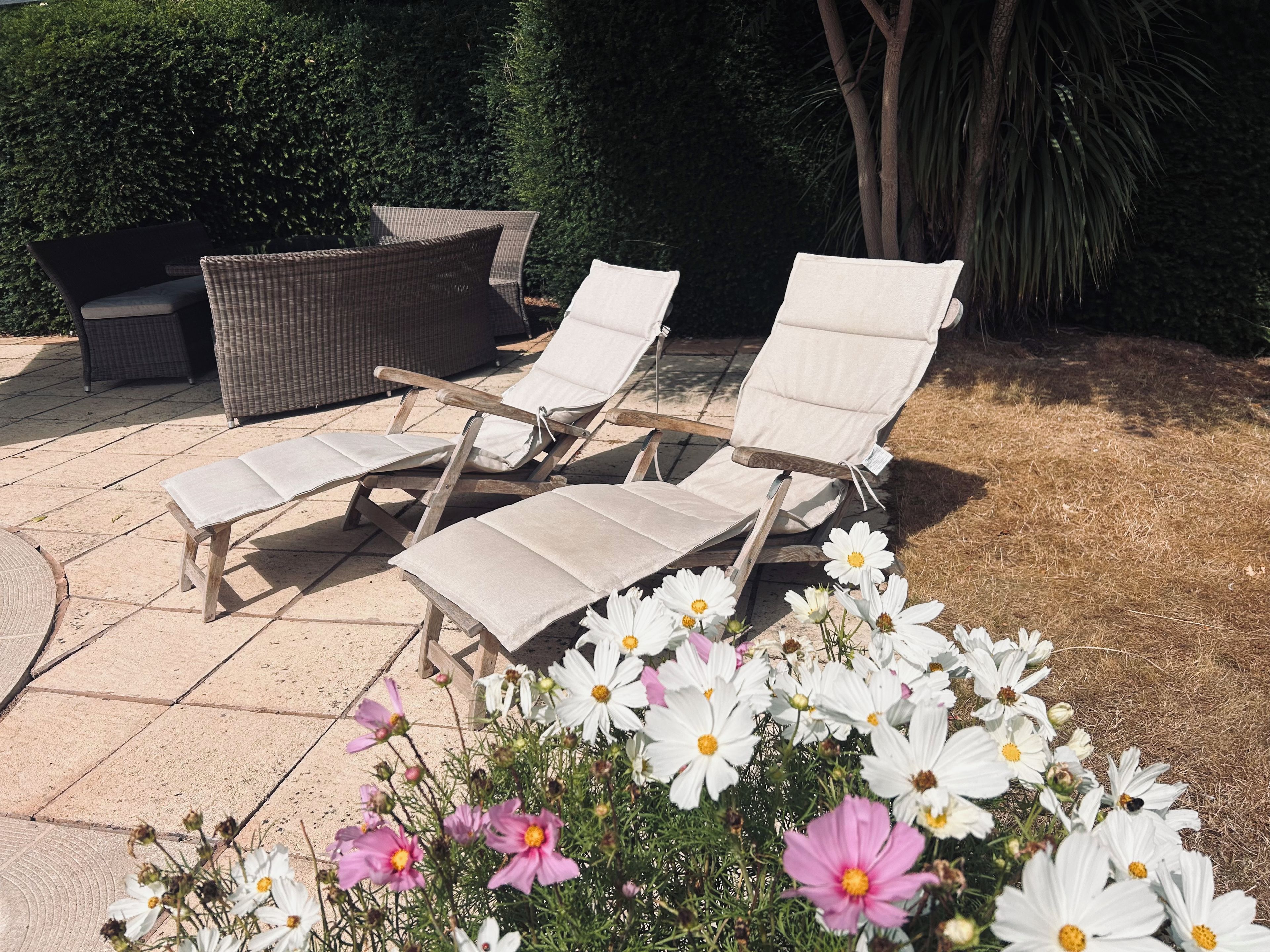 Des fauteuils de jardin, un canapé en osier et un parterre de fleurs avec des marguerites.