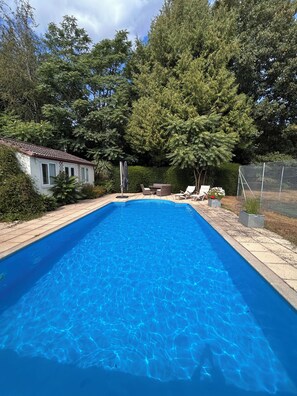 A rectangular swimming pool with clear blue water, surrounded by a paved deck.