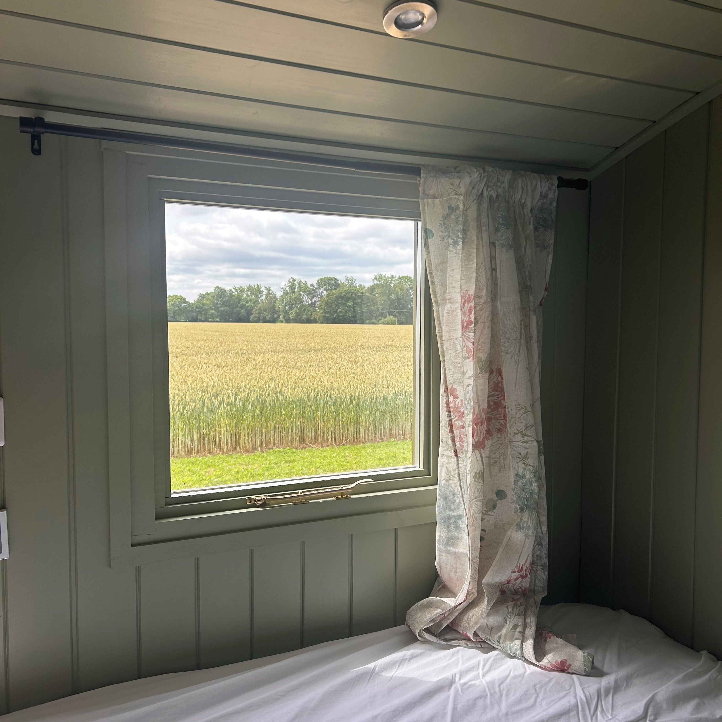 Une chambre avec un lit simple, une fenêtre avec un rideau et une vue sur un champ.
