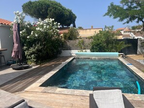 A rectangular swimming pool with a wooden deck surrounding it, a lounge chair, and a patio umbrella. - Luxurious villa with a pool, close to the beaches and the harbor. (Saint-Cyprien)