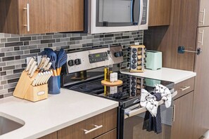 Una cocina moderna con estufa de acero inoxidable, un microondas encima y un bloque de cuchillos en la encimera.