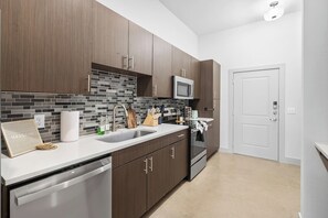 A modern kitchen with dark wood cabinets, a stainless steel sink, and a microwave. - Cozy Lux 1BR 1BA in Dallas | Mins to DT | Free Parking (Dallas)