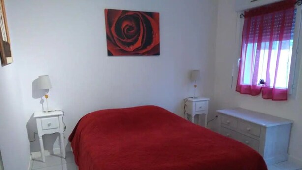 A bedroom with a bed, a nightstand, a dresser, a window with curtains, and a wall-mounted artwork. - A LITTLE CORNER OF THE GARD PROVENCAL (Saint-Gilles)