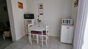 A small, clean room with a white table and chairs, a microwave, a radio, and a framed picture on the wall. - A LITTLE CORNER OF THE GARD PROVENCAL (Saint-Gilles)