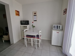 Ein kleines, sauberes Zimmer mit einem weißen Tisch und Stühlen, einer Mikrowelle, einem Radio und einem gerahmten Bild an der Wand.