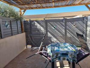 Eine überdachte Terrasse mit Tisch und Stühlen, ein Pergola darüber und ein Zierzaun mit Schmetterlingsdekorationen.