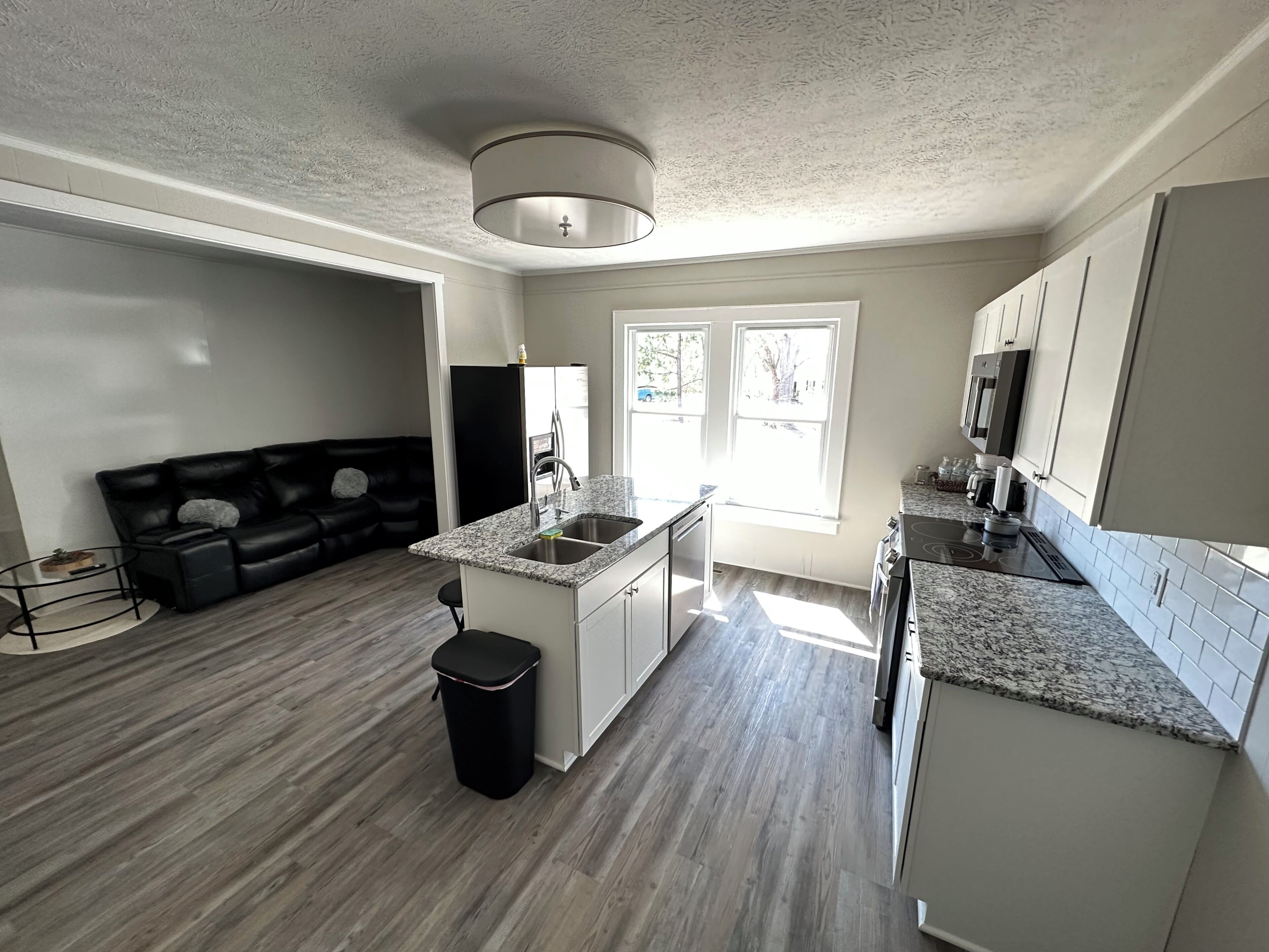 A modern kitchen with granite countertops, stainless steel appliances, and a black trash bin.