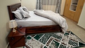 A bedroom with a bed, a nightstand, a lamp, a wardrobe, and a patterned rug. - Perfect 2-bedroom apartment with AC in enjoyable Kampala (Kampala)