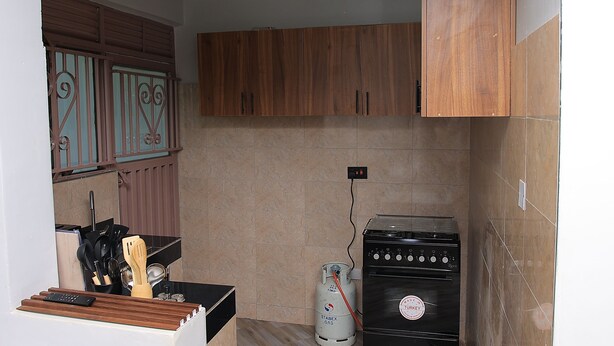 A compact kitchen with wooden cabinets, a gas stove, and a gas cylinder. - Perfect 2-bedroom apartment with AC in enjoyable Kampala (Kampala)