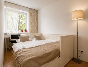 Ein Schlafzimmer mit Bett, Nachttisch, Lampe, Fenster mit Blick und einem Schreibtisch mit Stuhl.