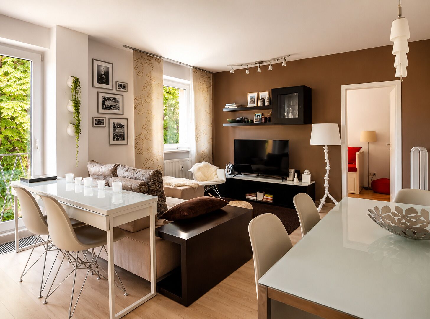 Een moderne woonkamer met een flatscreen-tv, een eethoek met een witte tafel en stoelen, en een gezellige zithoek met een bank en kussens.