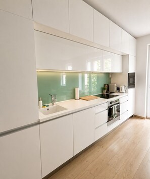 A modern kitchen with white cabinetry, a green backsplash, and a wooden countertop. - Bright Central 2BR Business & City Stay - Nivy - Balcony - Fast WiFi (Bratislavský kraj)