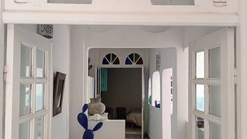 A hallway with white doors, a blue cactus sculpture, and a patterned floor leading to a bedroom.